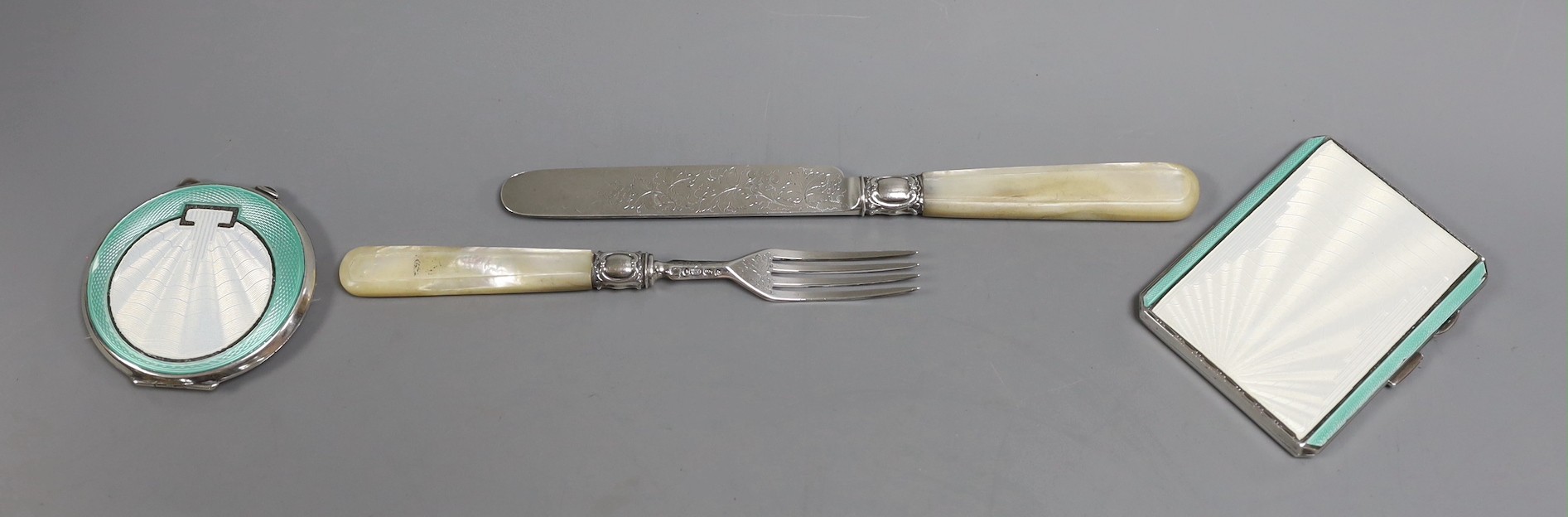 Two Art Deco silver and two colour enamel compacts, largest 85mm and a Victorian mother of pearl handled silver christening knife and fork.